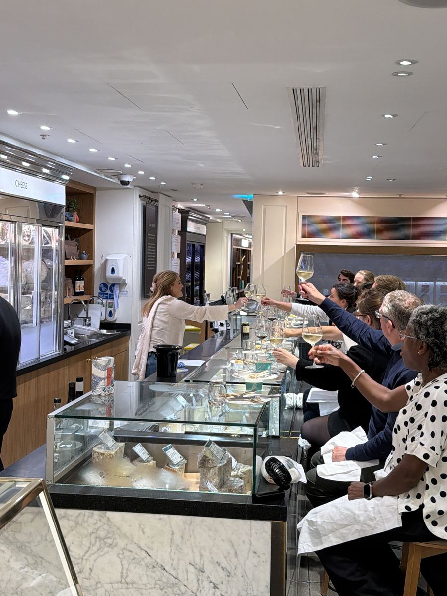 Guests seated along the cheese counter raise glasses of white wine to Morgan McGlynn Carr at a Cheese Lates evening in the Fortnum & Mason Food Hall