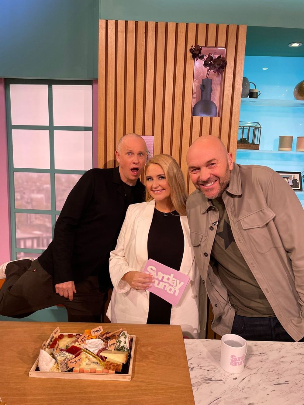 Morgan McGlynn Carr with presenters Tim Lovejoy and Simon Rimmer on the set of Channel 4's Sunday Brunch, with a cheeseboard on the counter